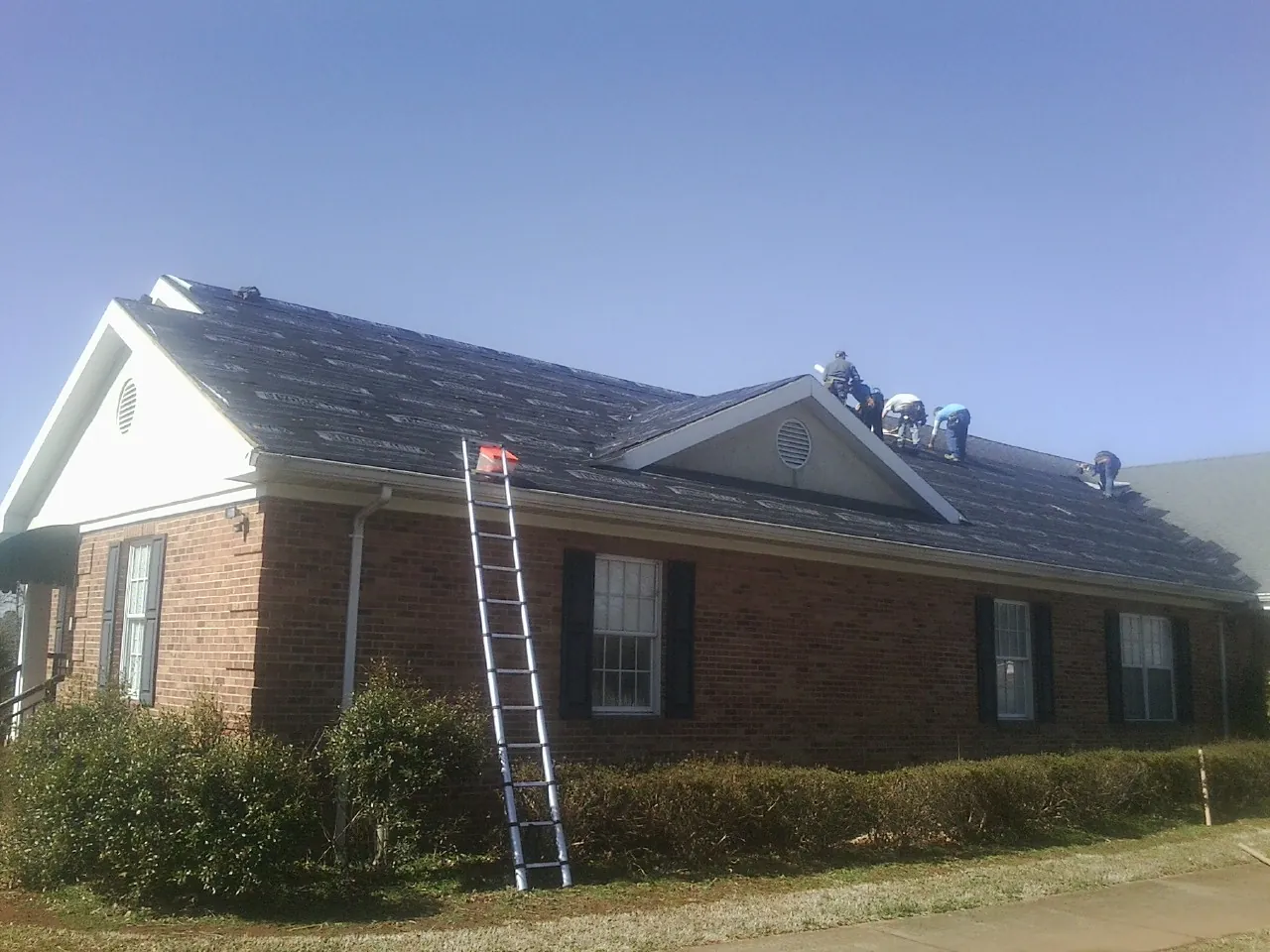 Crew tearing shingles off a brick ranch roof with a ladder set — Emergency Roof Repair work by our crew in Manhattan