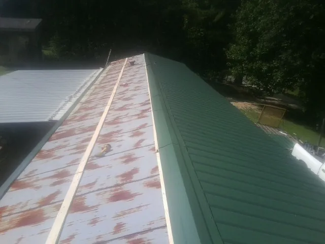 Old rusted panels beside newly installed green metal roofing — Wind Damage Roof Repair by Roofing Brothers in Manhattan