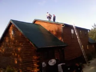Crew on the ridge of a green metal roof on a two story log home in Manhattan