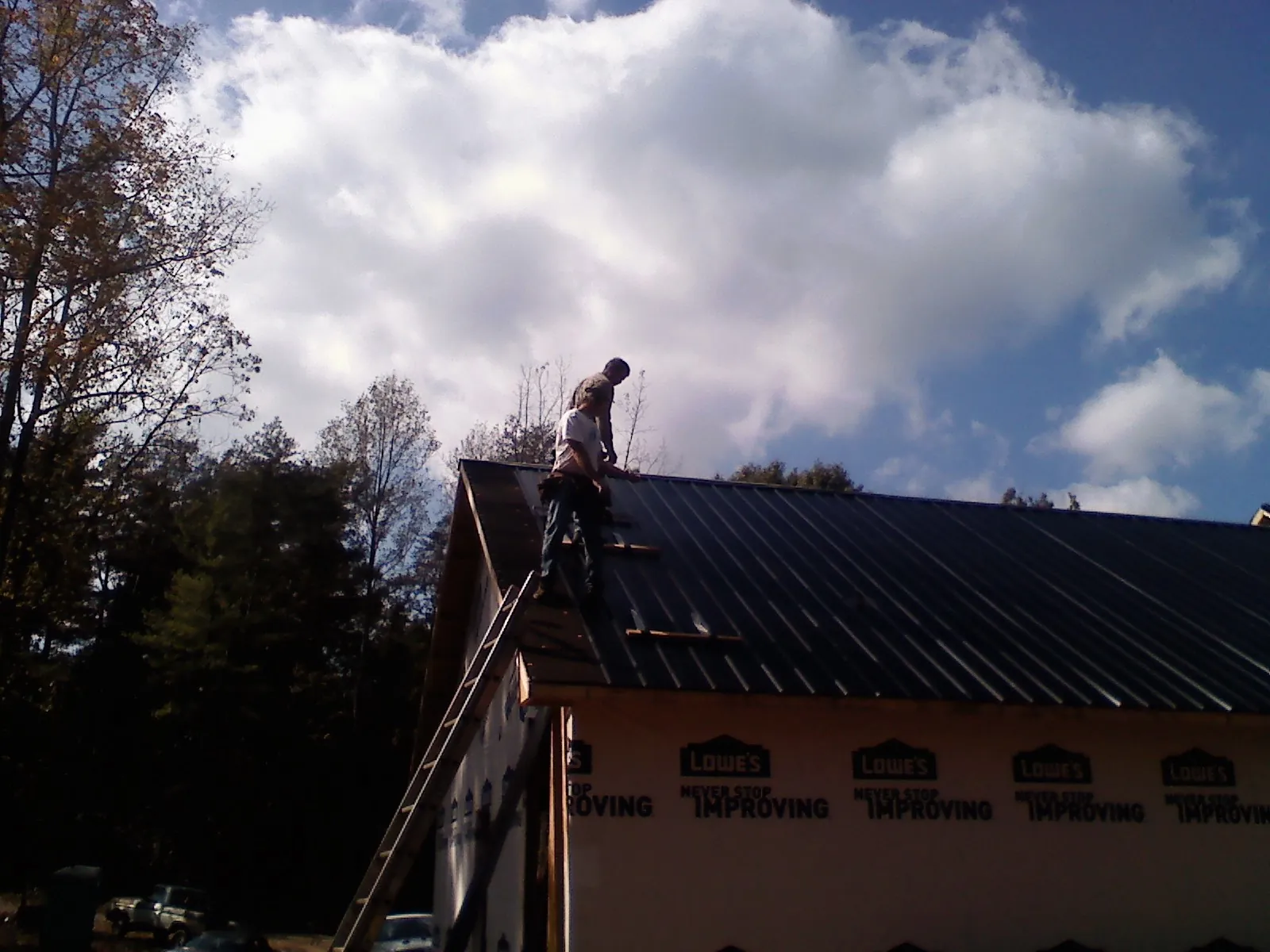Roofer fastening dark metal panels high against a cloudy sky, from a Roof Inspection job in Manhattan