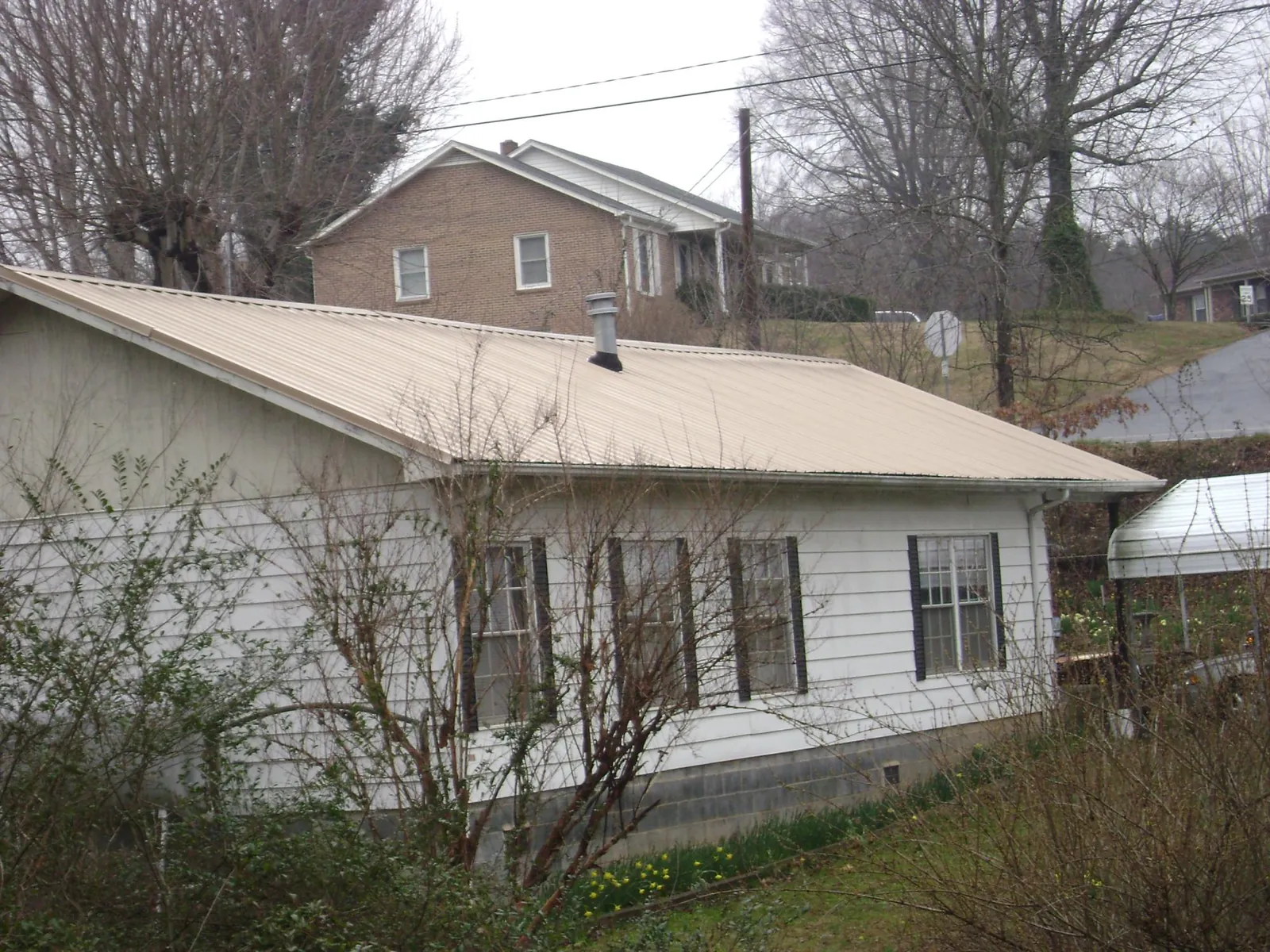 Tan metal roof on a white sided house set into a hillside — Commercial Roofing by Roofing Brothers in Manhattan
