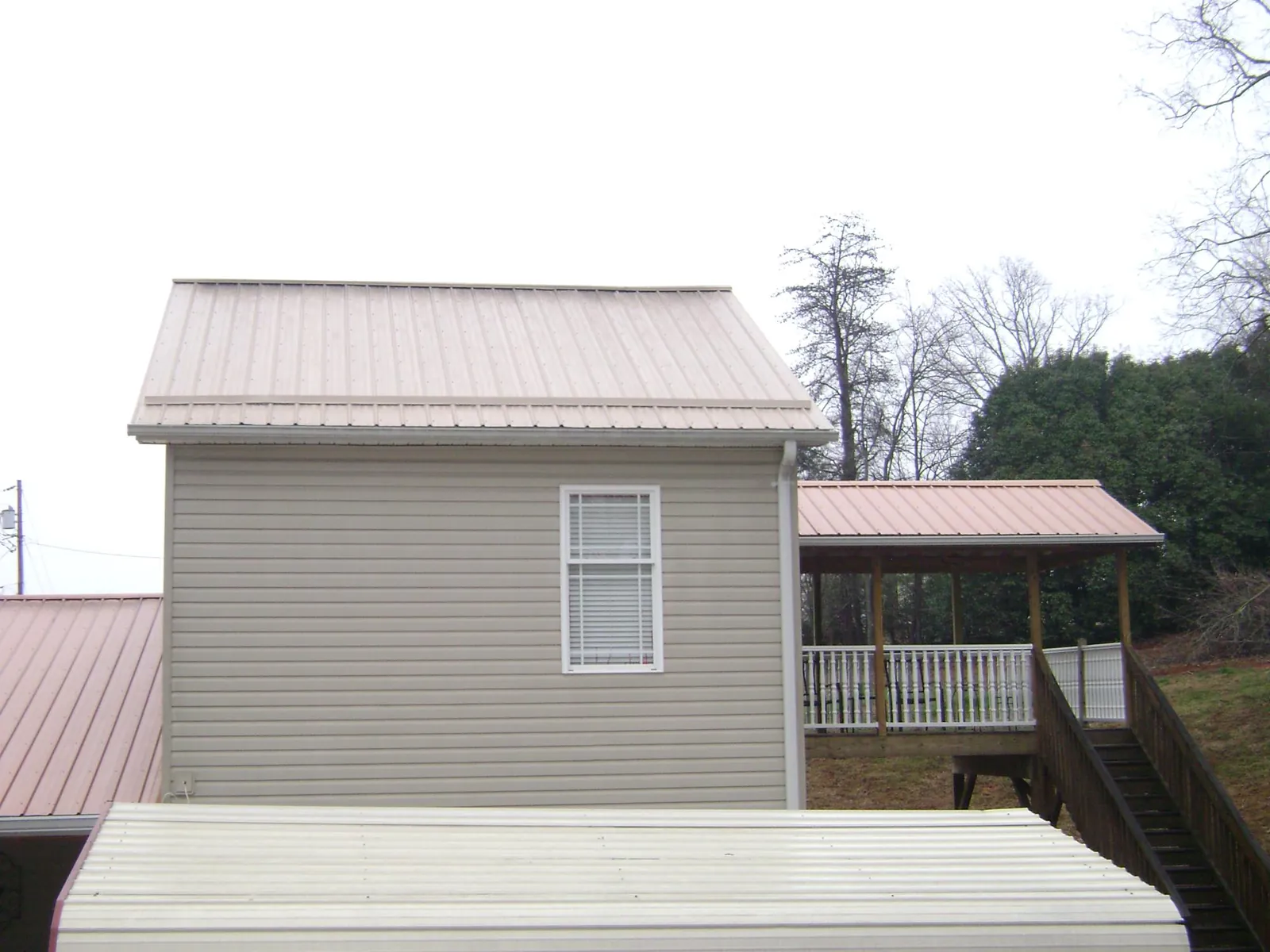 Tan metal roofs on a two story addition and attached porch, from a Roof Replacement job in Manhattan